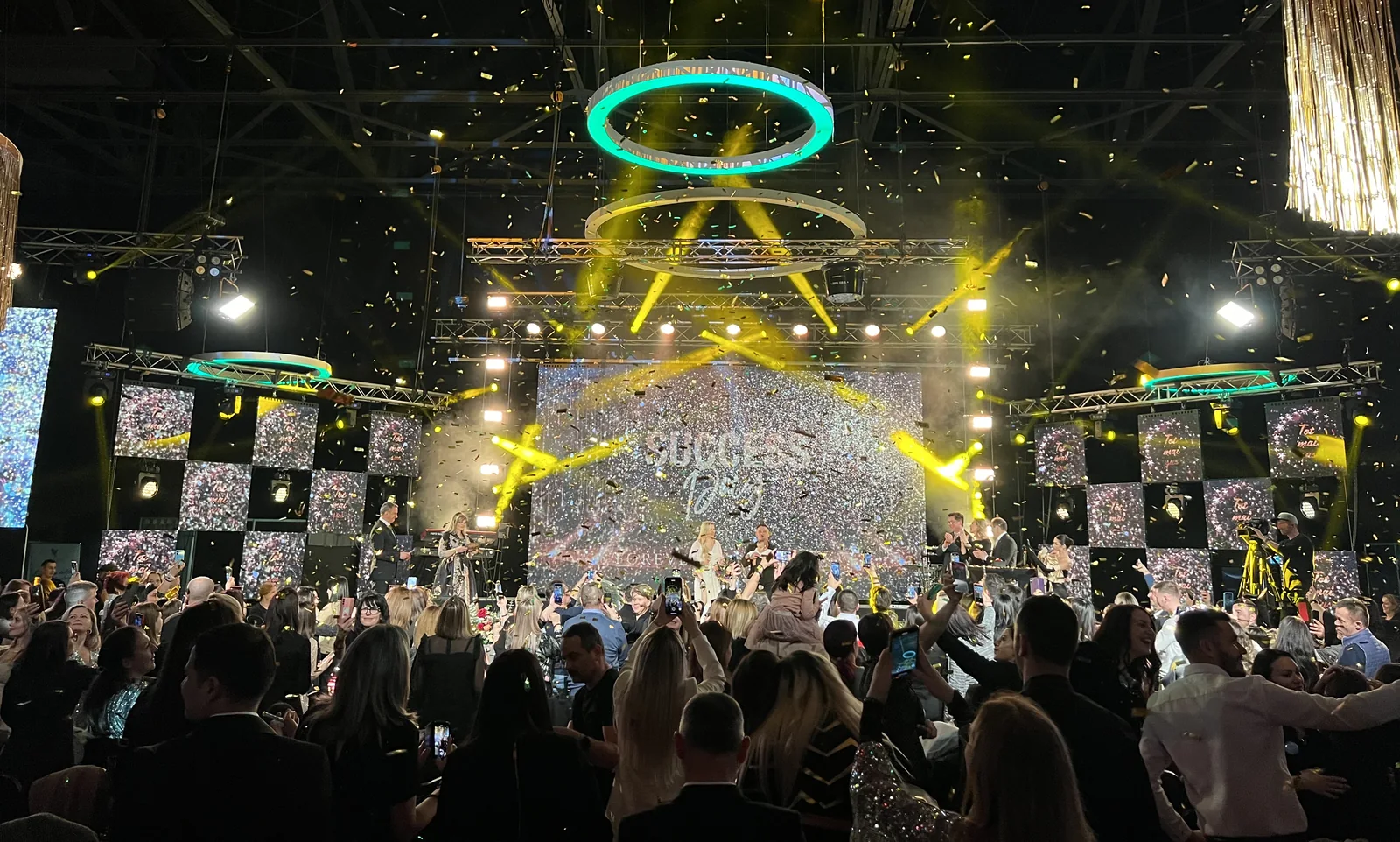 Petrecere corporate cu public, scenă, ecrane, confetti și lumini de spectacol